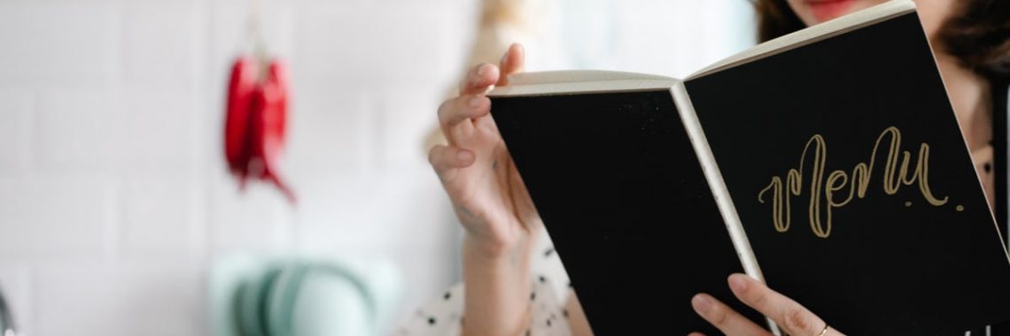 Close-up of a woman reading a menu indoors with a blurred cozy kitchen background.